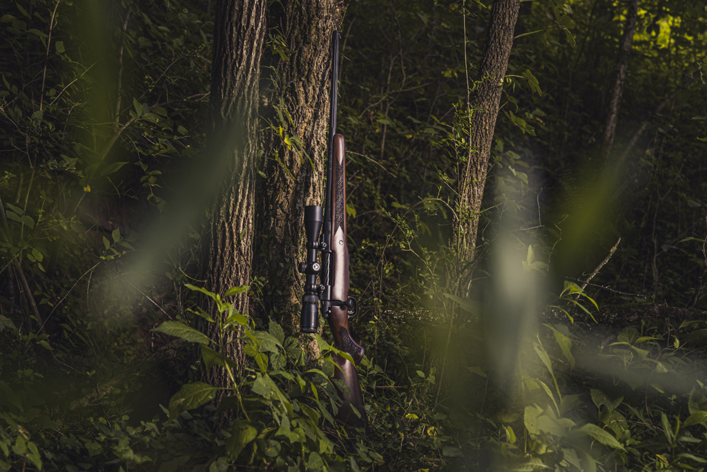 a photo of a hunting rifle leaning against a tree in a forrest