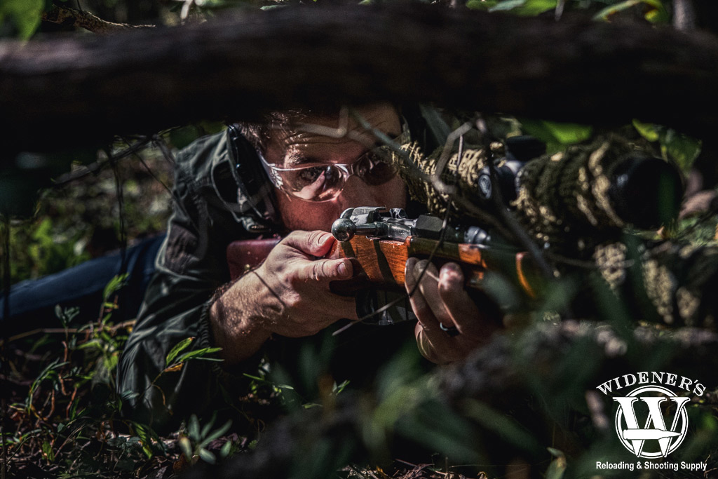 a man posing in the woods with a sniper rifle A photo of a man posing in the woods with a sniper rifle
